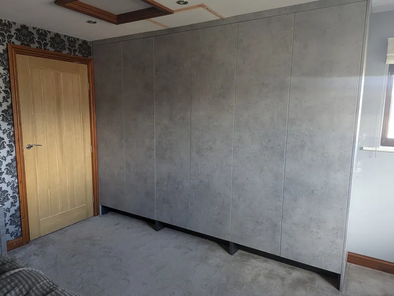 Full-height fitted wardrobes in a stone-effect finish filling a bedroom wall
