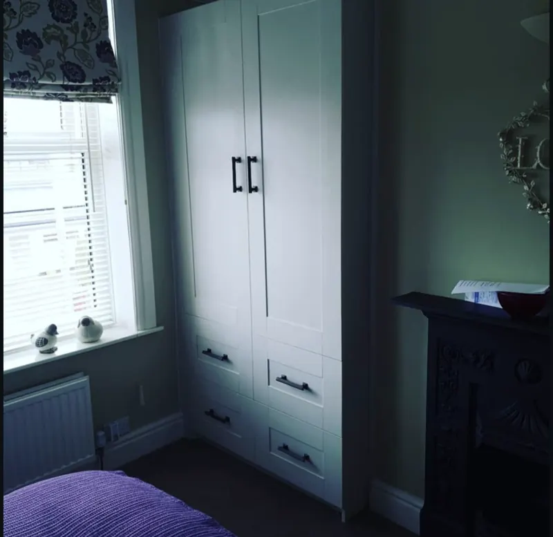 Painted alcove cupboard with drawers beside a fireplace