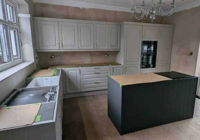 Kitchen part way through fitting, with painted units and a dark island before the worktops