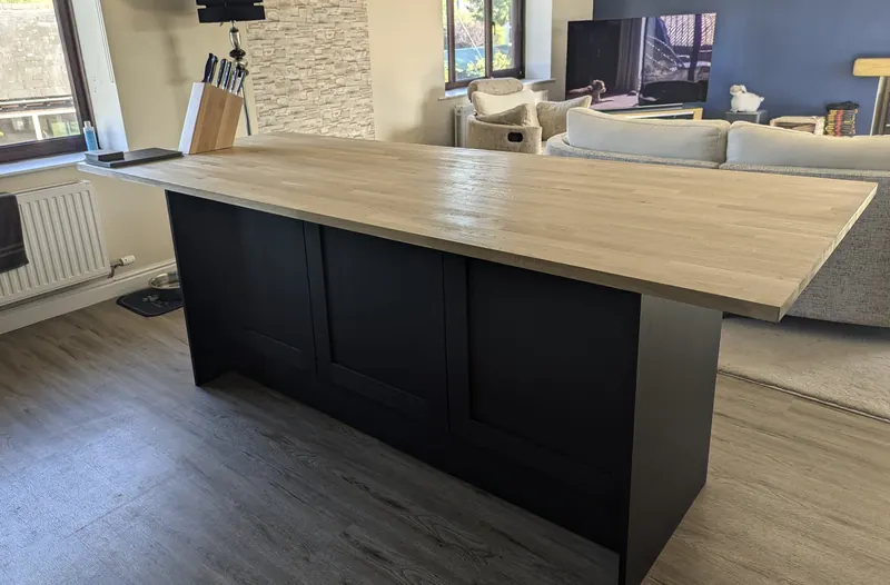 Kitchen island with a dark painted base and a long oak worktop in an open-plan room