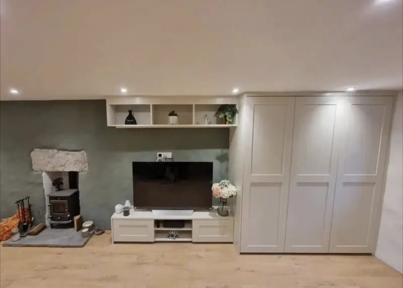 Living room with a painted fitted cupboard, TV unit and open shelving beside a wood burner